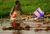 A Songhai woman kneeling in mud washing clothes in the Niger River, Gao, Mali, West Africa
