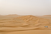 A jeep drives over sand dunes in the Empty Quarter, Ar Rub Al Khali, Oman.
