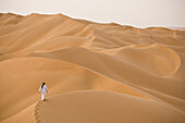 A man walks alone on the sand dunes of the Empty Quarter, Ar Rub Al Khali, Oman.