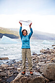 TORRES DEL PAINE NATIONAL PARK, PATAGONIA, CHILE. A smiling woman holds a piece of ice, which fell from a glacier, while standing on the rocky shore.