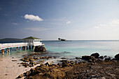 A dock extends over the clear, blue and green waters of the Caribbean on a sunny day.