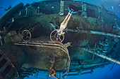 A woman blows bubble-rings while freediving (breah-hold diving) underwater on the side of the Kittiwake Shipwreck off Grand Cayman Island.