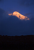 The North Face of Mount Everest shines above the stark Himalayan landscape at dusk. Rongbuk Glacier, Tibet.