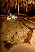 Cave explorer Syria Lejau looks into a very pretty Gour Pool. The floor of which is covered with 'dog tooth' crystals. The edges of the pool are very fragile because they overhang so much. These pools were discovered on this latest expedition and are loca