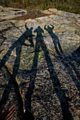 Three friends make shadow art on the granite top of  Cadillac Mountain in Acadia National Park, Maine.