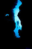 Silhouette of Daniel Brown at Coral Canyons at Chub Hole Dive Site, East End, Grand Cayman, British West Indies. The diver peers through the fissure in the coral wall in anticipation of the unknown.