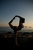 Frau übt Yoga an der Küste von Maine bei Sonnenuntergang, New England.