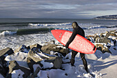 Carrying his surfboard, Akin Franciscone strikes out through snow-covered boulders towards cold winter surf in Homer, Alaska on January 26, 2006.