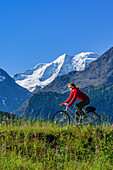 Woman cycling, Piz Palue in background, Samedan, Upper Engadin, Engadin, Canton of Graubuenden, Switzerland