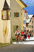 Cyclists riding along cobbled street, Guarda, Lower Engadin, Canton of Graubuenden, Switzerland