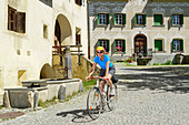 Radfahrerin fährt über Kopfsteinpflaster, Guarda, Unterengadin, Engadin, Kanton Graubünden, Schweiz