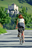 Fahrradfahrerin auf einer Landstraße, Schloss Tarasp im Hintergrund, Ftan, Unterengadin, Engadin, Kanton Graubünden, Schweiz