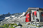 Woman standing in front of alpine hut, granite mountains in background, bivouac Kima, Sentiero Roma, Bergell range, Lombardy, Italy
