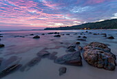 Long exposure of a pink sunset at the beach during dusk with rocks in the foreground, Tangalle, Sri Lanka, Asia