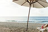 Beach umbrella on beach, semi-naked person lying on deckchair