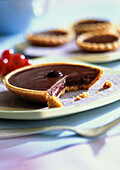 Chocolate and red currant tartlets, one in foreground with bite missing, close-up