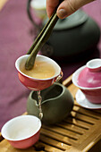 Tea cup held with tea tongs, pouring out first brew into tea tray