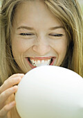 Young woman blowing up balloon, laughing, close-up