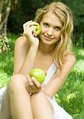 Young woman sitting in grass, holding up apples
