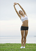 Young woman doing stretching exercises by lakeside