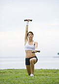 Young woman working out with weights by lakeside