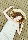 Woman lying on deck, wrapped in towel, head on mat