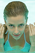 Young woman in pool, hands by side of face and face dripping