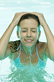 Young woman in pool, splashing face with water
