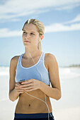 Young woman using MP3 player on beach, wearing active wear