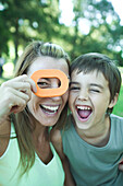 Boy and mother, woman looking through toy shape, both laughing and looking at camera
