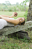 Woman lying on piece of wood, holding apple, looking at camera
