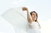 Woman outdoors, holding shawl in wind, looking away, low angle view