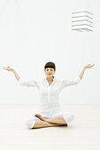 Woman sitting in lotus position with eyes closed, hands raised