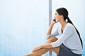 Woman sitting with legs up, talking on cell phone, looking out window