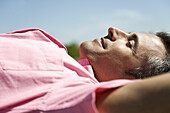 Man lying outdoors in sun with hands behind head