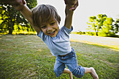 Parent spinning little boy in park, cropped