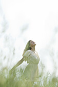 Young woman in field of tall grass, standing with head back and eyes closed