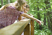 Mother and young daughter looking over railing together