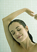 Woman taking shower, arms up and eyes closed