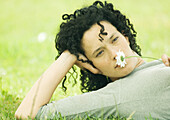 Woman lying on ground and holding daisy to nose