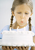 Little girl holding birthday cake, blowing out candles