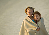 Two girls wrapped in towel together at beach