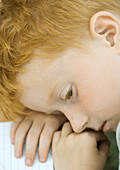 Boy with head down on table next to notebook, high angle view