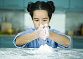 Girl standing at kitchen counter, holding hands over pile of flour