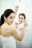 Woman holding shower curtain open where friend is taking shower