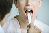 Doctor holding down woman's tongue with tongue depressor