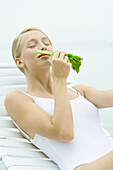 Teenage girl wearing bathing suit, sitting in lounge chair, smelling celery stalk