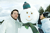 Brother and sister leaning against snowman, sister whispering, brother listening