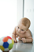 Baby on floor, looking at ball in blurred foreground