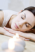 Woman reclining next to burning candles, head resting on arms, eyes closed